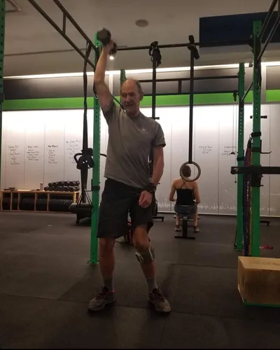 A trainer performing an overhead dumbbell press using a resistance strap attached to a squat rack