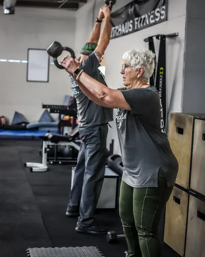Two clients performing overhead kettlebell swings together in the gym