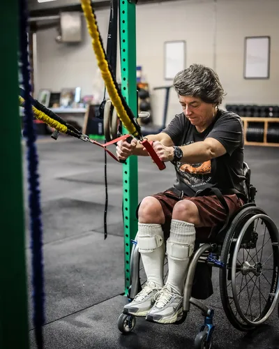 A wheelchair athlete performs a seated resistance band pull at a cable station
